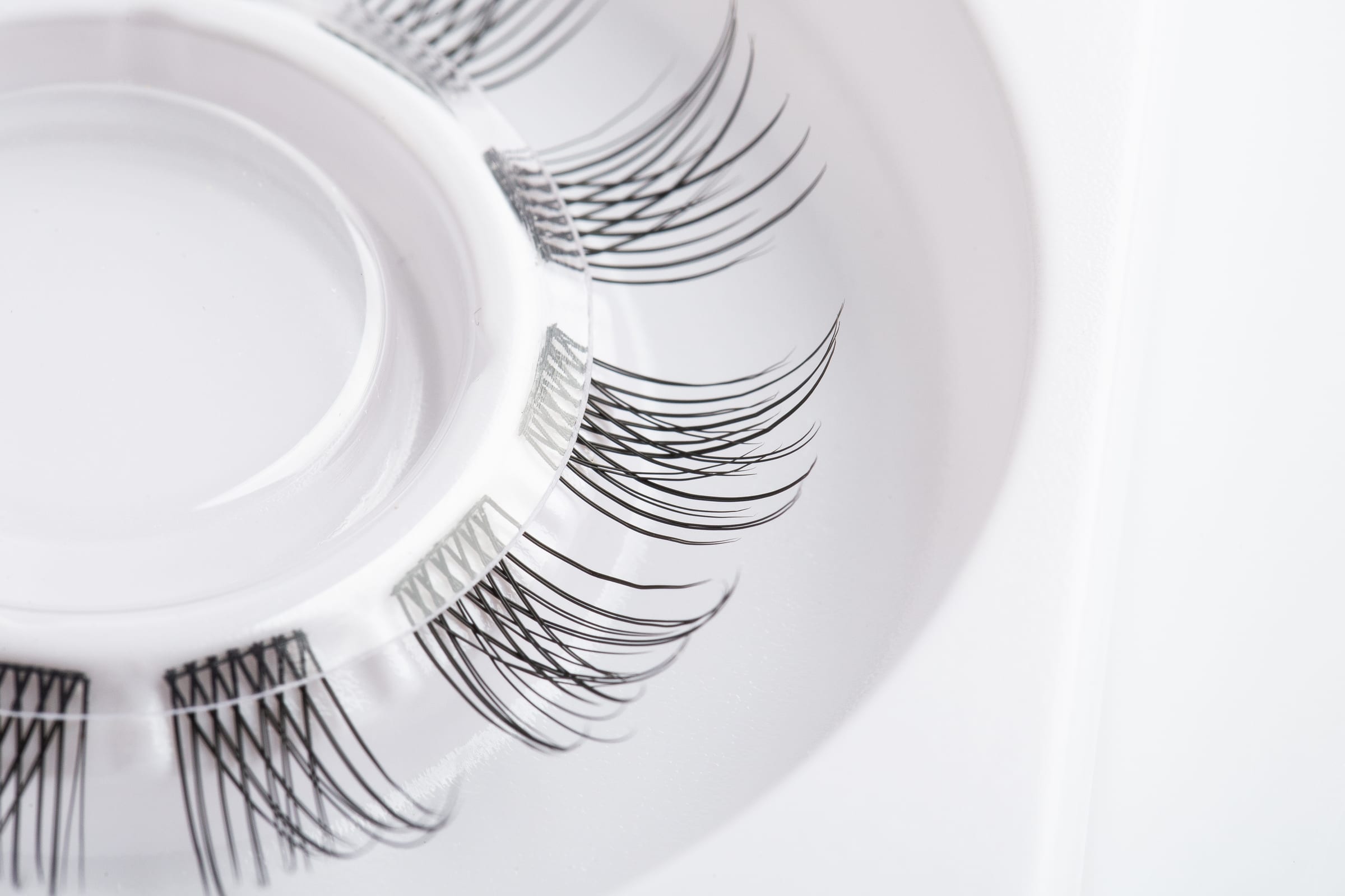Original close-up photograph of fine black DIY lash segments on a white product tray